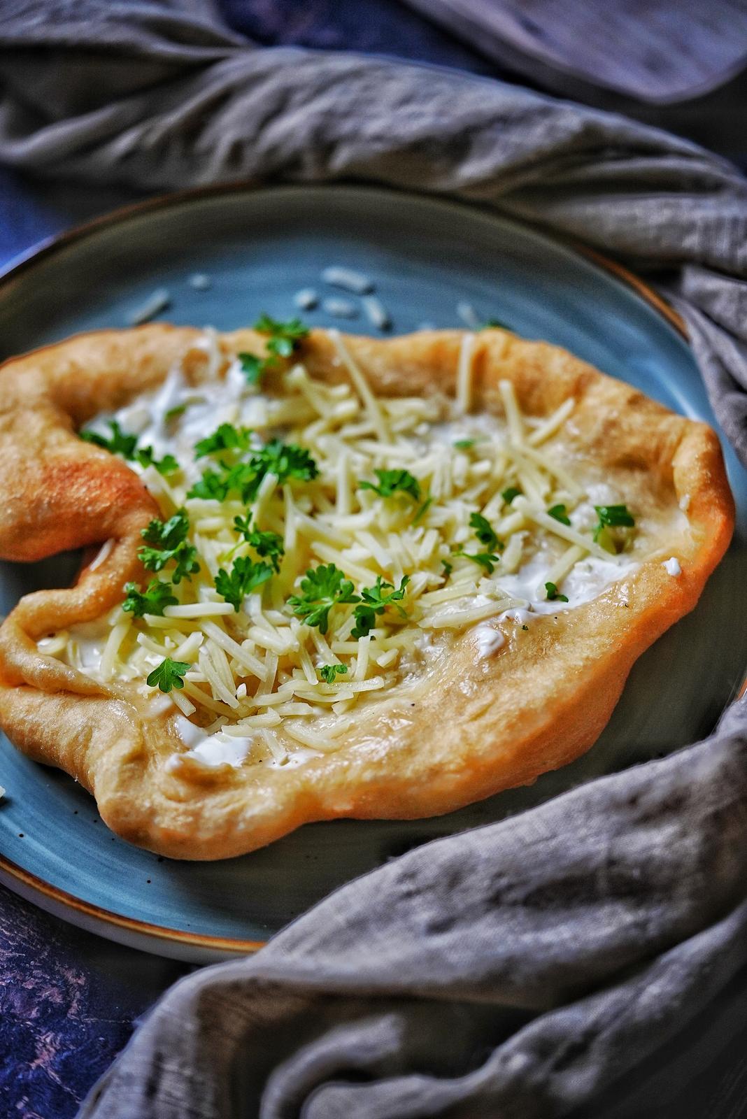 Frisch gebackener Langos mit Sauerrahm, Käse und Petersilie auf einem Teller