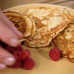 rei goldbraune Pancakes mit Himbeeren auf einem hellen Teller