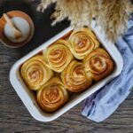 Frisch gebackene Sauerteig-Zimtschnecken in einer weißen Auflaufform auf Holztisch