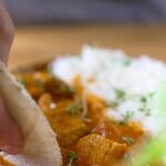 Butter Chicken mit Reis und Fladenbrot serviert